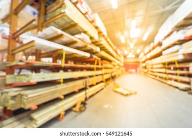 Blurred Stack New Wooden Bar On Shelves Inside Lumber Yard Of Large Hardware Store In America. Rack Of Fresh Mill/cut Wood Timber With Flatbed Cart, Manual Forklift In Warehouse. Industrial Background