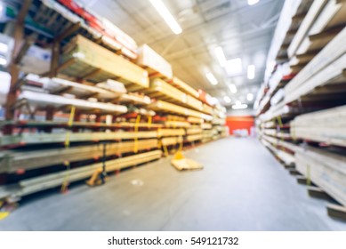 Blurred Stack New Wooden Bar On Shelves Inside Lumber Yard Of Large Hardware Store In America. Rack Of Fresh Mill/cut Wood Timber With Flatbed Cart, Manual Forklift In Warehouse. Industrial Background