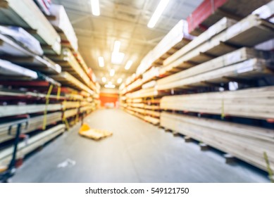 Blurred Stack New Wooden Bar On Shelves Inside Lumber Yard Of Large Hardware Store In America. Rack Of Fresh Mill/cut Wood Timber With Flatbed Cart, Manual Forklift In Warehouse. Industrial Background