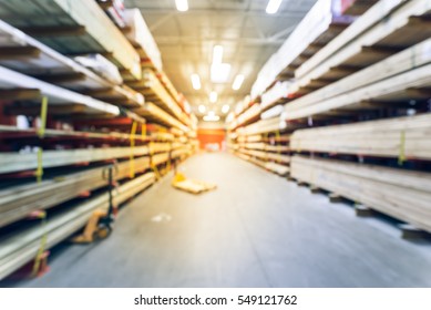 Blurred Stack New Wooden Bar On Shelves Inside Lumber Yard Of Large Hardware Store In America. Rack Of Fresh Mill/cut Wood Timber With Flatbed Cart, Manual Forklift In Warehouse. Industrial Background