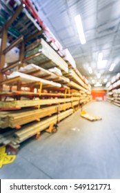 Blurred Stack New Wooden Bar On Shelves Inside Lumber Yard Of Large Hardware Store In America. Rack Of Fresh Mill/cut Wood Timber With Flatbed Cart, Manual Forklift In Warehouse. Industrial Background