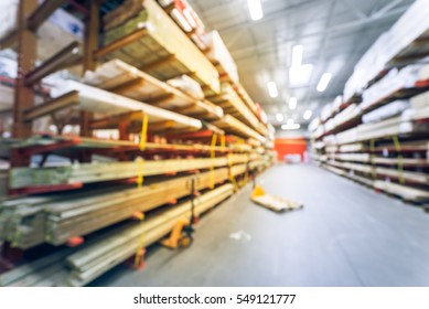 Blurred Stack New Wooden Bar On Shelves Inside Lumber Yard Of Large Hardware Store In America. Rack Of Fresh Mill/cut Wood Timber With Flatbed Cart, Manual Forklift In Warehouse. Industrial Background