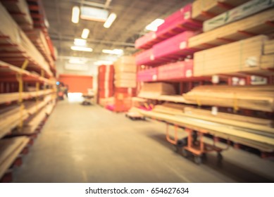 Blurred Stack New Wooden Bar On Shelves Inside Lumber Yard Of Large Hardware Store In America. Rack Of Fresh Mill/cut Wood Timber With Flatbed Cart, Manual Forklift In Warehouse. Industrial Background