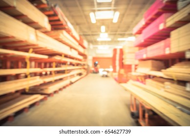 Blurred Stack New Wooden Bar On Shelves Inside Lumber Yard Of Large Hardware Store In America. Rack Of Fresh Mill/cut Wood Timber With Flatbed Cart, Manual Forklift In Warehouse. Industrial Background