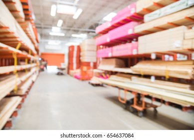 Blurred Stack New Wooden Bar On Shelves Inside Lumber Yard Of Large Hardware Store In America. Rack Of Fresh Mill/cut Wood Timber With Flatbed Cart, Manual Forklift In Warehouse. Industrial Background