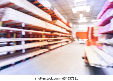 Blurred Stack New Wooden Bar On Shelves Inside Lumber Yard Of Large Hardware Store In America. Rack Of Fresh Mill/cut Wood Timber With Flatbed Cart, Manual Forklift In Warehouse. Industrial Background