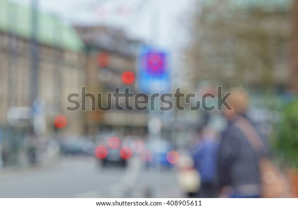 Blurred street scene in a city center.\
Un-focused unidentifiable person close to traffic sign. Historic\
buildings, cars and traffic lights in the\
background.