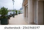 Blurred street scene in monaco with luxury vibe featuring potted plants, elegant columns, and defocused cars creating a sophisticated outdoor atmosphere.