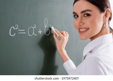 Blurred teacher smiling at camera while writing mathematic formula