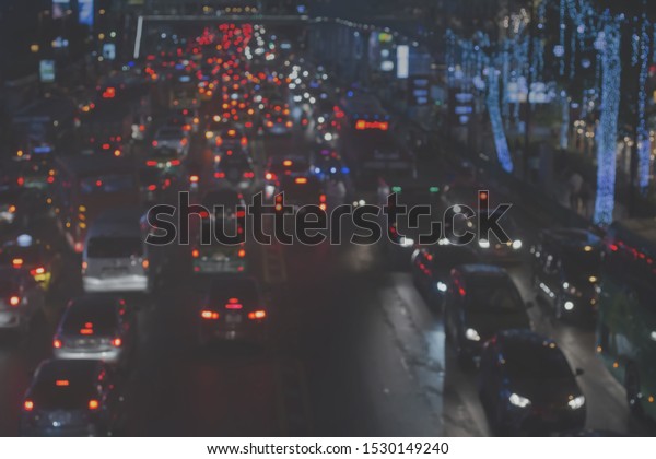 Blurred traffic jam and smoke or haze in Bangkok\
Thailand background. Abstract blurry image midnight lighting bokeh\
of red tail lamp and brightness headlamp from many vehicles slowly\
drive on road.