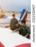 Blurred training photo with sunset effect. Pilot trainer in green uniform teaching about Aircraft flying system and wings with 2 flyer students near white airplane.