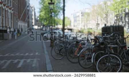 Blurred view of bicycles lining the amsterdam canal street with people and classic architecture suggesting vibrant city life and travel in the netherlands.