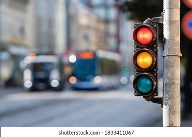 blurred view of city traffic with traffic lights, in the foreground a semaphore with a red and yellow light - Shutterstock ID 1833411067