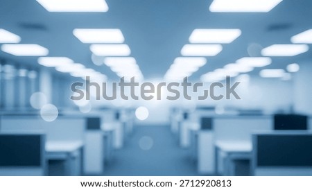 A blurred view of empty office cubicles, desks and chairs in a workspace.