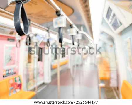 Blurred view of an empty subway train interior with bright yellow seats and stainless steel poles. The modern train car is well-lit, featuring overhead handles and smooth