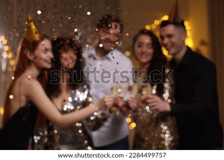 Blurred view of happy friends clinking glasses of sparkling wine at birthday party indoors