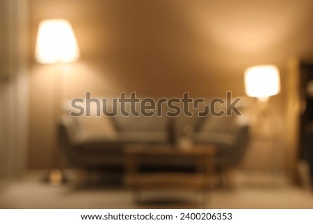 Blurred view of modern living room with grey sofa, coffee table and glowing lamps at evening