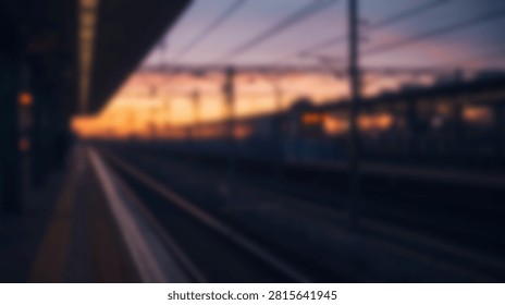 A blurred view of a train station platform during a vibrant sunset, with tracks stretching into the distance and overhead wires visible against the colorful sky.