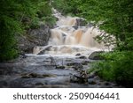 The blurred water of Duchesnay Falls flows down a river through a forest in North Bay, Ontario during sunset.