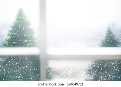 Blurred window glass with snow fall and pine trees in winter  season.For new year and christmas day background.