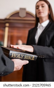 blurred woman giving oath on bible in hand of bailiff in courtroom