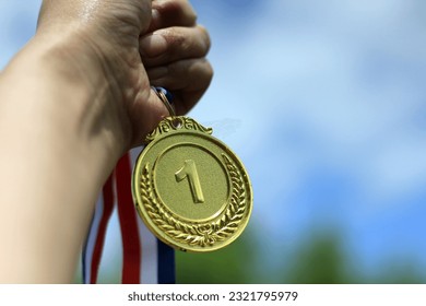 Blurred of woman hands raised and holding gold medals with ribbon against blue sky background to show success in sport or business, Winners success award concept.