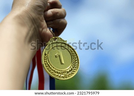 Blurred of woman hands raised and holding gold medals with ribbon against blue sky background to show success in sport or business, Winners success award concept.