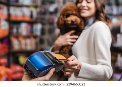 Blurred Woman Holding Poodle And Paying With Credit Card In Pet Shop 