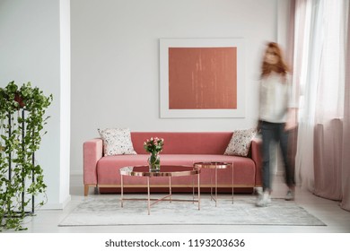 Blurred Woman Walking In A Feminine Living Room Interior With A Sofa, Coffee Table And Painting