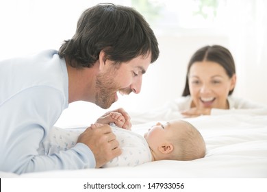 Blurred young woman looking at happy man play with baby in bed at home