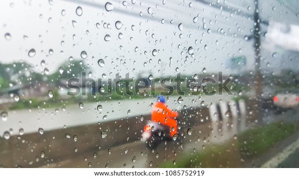 Blurred-The view\
through the glass, the raindrops and the men in the orange rain\
suit, riding the motorcycle on the wet road, in the rain dew. On a\
rainy day, Blur in the\
background.