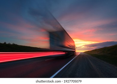 Blurring. A Large Truck Is Driving Along The Highway At High Speed. Sky With Bright Red Clouds. Delivery Of Cargo.