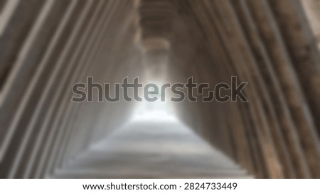 A blurry abstract perspective looking up inside a tall geometric stone monument towards a bright opening at the apex