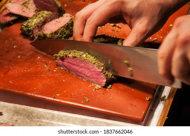 Blurry Background Chef Slice Loin Of Venison On Brown Board In Restaurant Kitchen.