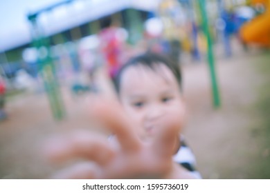 Blurry Background Image Of Little Kid Reaching Hand To Camera In A Park Alone, Out Of Focus Photo Of Small Child Reach Hand To Grab Camera, Space For Text And Design