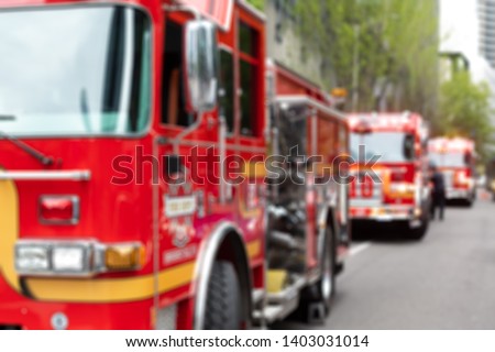 Blurry background of modern red firetrucks parked along a city street, in a first responder scene with space for text on the right