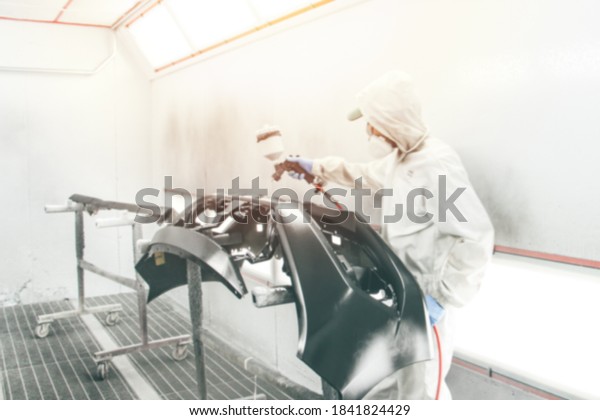 Blurry background Repairman painter
hand in protective glove with hand holding airbrush sprinkler
painting car body in a paint chamber during repair
work