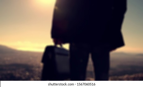 Blurry Background From Silhoutte Of Young Businessman Holding Briefcase And Look Town View As A Market To Be Conquered In Future.