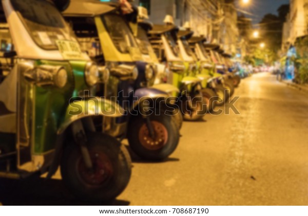 Blurry Background of Three-wheel taxi parked on\
the side of the road. In Thailand, Thailand nationals call these\
cars that \