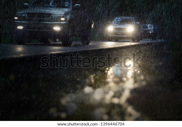 Blurry cars run through the dark mysterious forest\
during hard rain fall. 