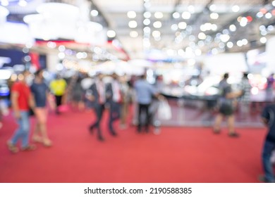 Blurry Crowd Visitors Walking In An Exhibition Event Hall. Bokeh Background Of Trade Show Business, World Or International Expo Showcase, Tech Fair, With Exhibitor Trade Show Booth Displaying Product.