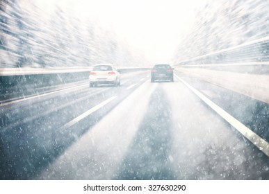 Blurry dangerous car overtaking on highway at heavy snowy conditions.