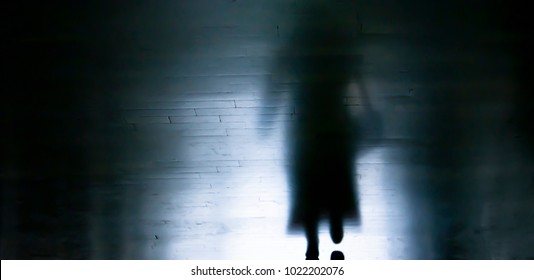 Blurry dark alley in the night with silhouette and shadow of a woman in long coat and high heels walking away