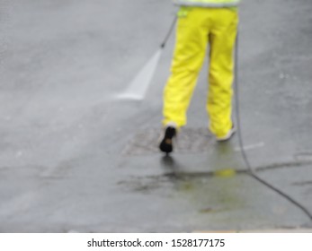 Blurry Defocus Image Of Man Using Jet Power Washer Hose To Clean Paint Off Road Surface. Road Cleaning With High Power Pressure Water Jet Hose