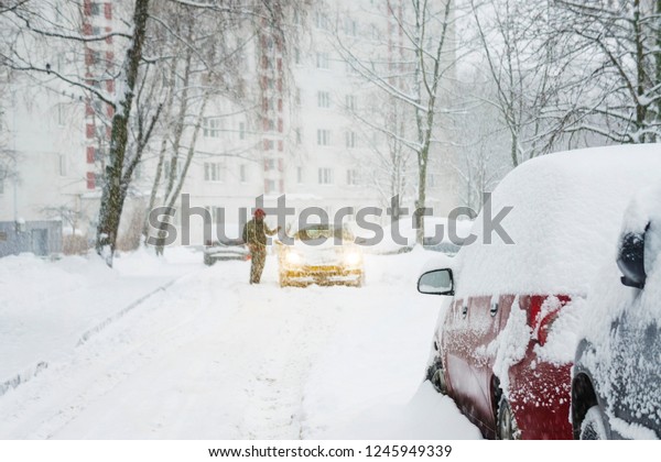 Blurry defocused background of silhouette of a\
man in a hood near his car with headlights on. Driver near his snow\
covered car. Snow trap\
concept