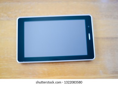 Blurry defocused close up of tablet pc mockup touch screen device laying on wooden desk. Modern wireless internet gadget flat lay topview copyspace. Work, watching video, game fun, texting design