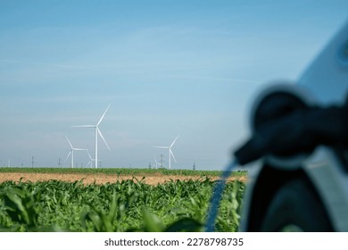 Blurry electric car charging through EV plug against windmills on corn field. Wind turbines generate renewable energy on unoccupied site - Shutterstock ID 2278798735