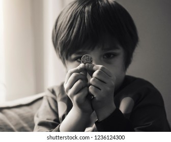 Blurry Face Of Kid Holding One Pound Coin In Black And White, Selective Fogus Of Unhappy Child Wearing Potty Shirt Showing One Pound For Donation Or Saving Money For Poor Kids