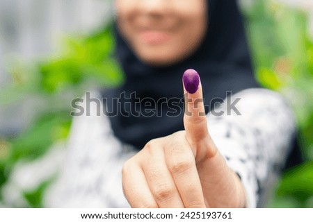 Blurry half face muslim girl showing pinky finger after voting on Indonesia presidential election. Election ads concept.