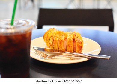 Blurry Iced Americano Black Cold Brew Coffee In Plastic Glass Grab Focused At Bakery (sausage Pie) In White Plate With Cutlery On Dark Wooden Table, Breakfast Set Before Go To Work Or School Concept